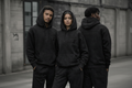 Three people wearing black hoodies with a brand logo, standing outdoors.